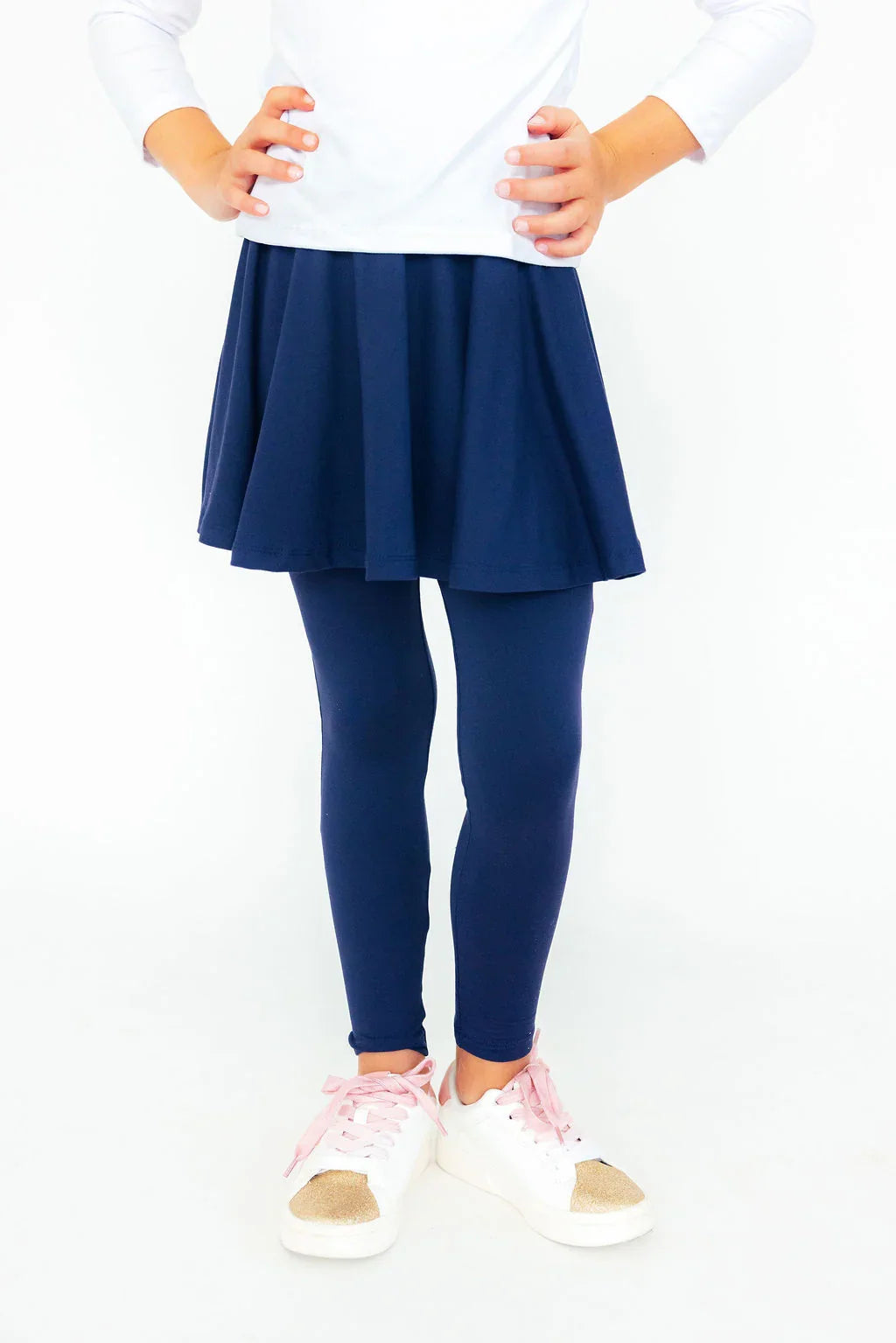 Little Girl wearing a navy skirt and leggings with white sneakers on a white background
