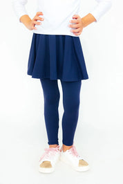 Little Girl wearing a navy skirt and leggings with white sneakers on a white background