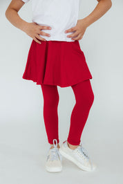 Kid wearing a white top, red skirt, and red leggings with white sneakers on a light gray background