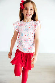 Young girl wearing a patterned top and red skirt with a white background