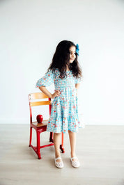 Young girl in a floral dress standing next to a chair with an apple on a white background