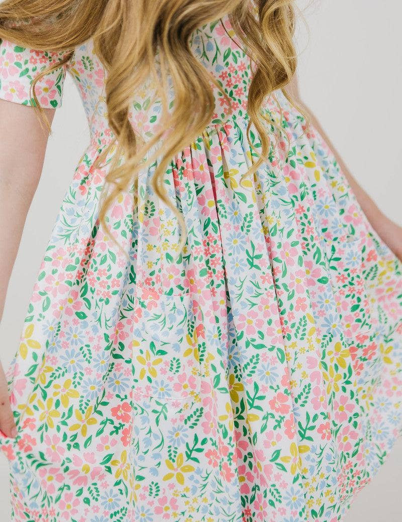 Girl wearing a daffodil print short sleeve twirl dress with pockets from JSQ Mercantile – a women’s boutique and gift shop in La Grange, IL.